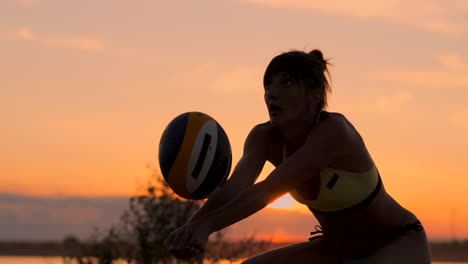 Middle-distance-volleyball-girl-in-bikini-waiting-for-the-ball-on-the-court-at-sunset-gives-forearm-pass-during-a-match-on-the-beach-in-slow-motion.